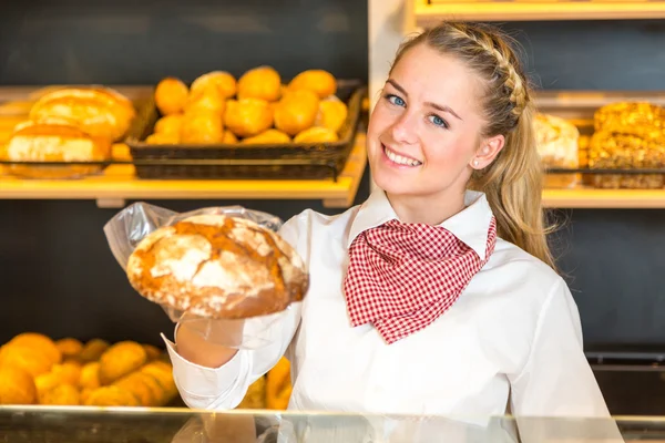 Shopkeeper in bakery presenting loaf of bread to client — Stock Photo, Image