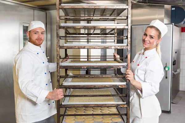 Twee bakkers poseren met plank met gebak in bakkerij Stockfoto