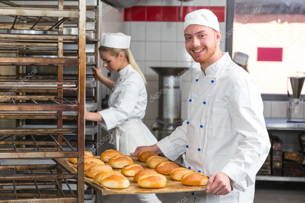 Baker presenting tray with pastry or dough at bakery