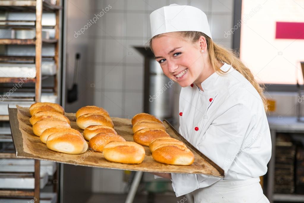 Baker or apprentice in bakery smelling fresh bread and buns