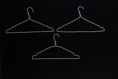 Fotoğrafta siyah bir arkaplanda elbise askılarının soyutlanmasını görebilirsiniz..