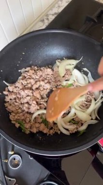 Top View Chef Hand 'in Ev Yapımı Lezzetli Lezzetli Yemekler Kızartması Kıymalı Kıymalı Et ile Sıcak Siyah Demir Tavada Dilimlenmiş Beyaz Soğan Tavasının Mutfak Fırınında Tahta Spatula Kullanımının Dikey Videosu