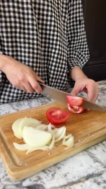 Mutfakta soğan ve domates gibi yiyecekleri hazırlarken ahşap tahtada sağlıklı ev yapımı ve mutlu ruh haliyle pişirme için taze sebze doğrayan mutlu kadının dikey videosu.