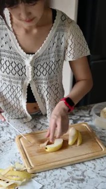 Evdeki Asyalı bir kadın için sağlıklı bir yaşam tarzı, sakin bir mutfak anının tadını çıkarmak ve basit besleyici beslenme için taze elma hazırlarken rahatlamaya odaklanmak.