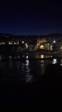 Dikey. Akşamları güzel Akdeniz köyü. Deniz kıyısındaki küçük bir kasabanın gece manzarası. İspanya 'da Calella de Palafrugell' in su ve ışıkları. Costa Brava tatili soğuk. Beyaz evler 