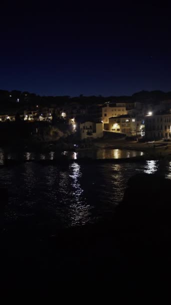 Vertikal. Indah desa Mediterania di malam hari. Pemandangan malam di kota kecil di pantai laut. Air dan lampu Calella de Palafrugell di Spanyol. Liburan Costa Brava yang dingin. Rumah putih — Stok Video