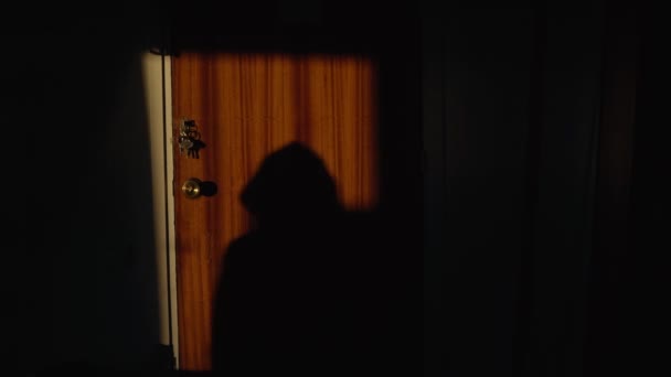 一个戴着头巾的男人在门上的可怕的影子。一个小偷试图打开门锁的轮廓。手伸向钥匙。可怕的。房子里的疯子偷东西的公寓。入室抢劫犯罪. — 图库视频影像