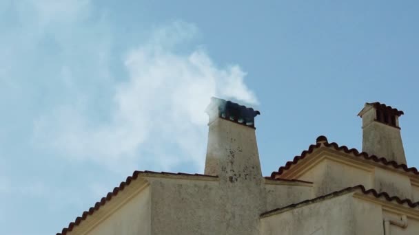 Rook uit de schoorsteen van een pittoresk oud huis in het dorp. Heldere winterdag. Mediterraan wit huis tegen de blauwe lucht. Open haard. Rook uit de keuken. Witte muren en een betegeld dak. — Stockvideo