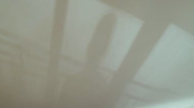 Tavanda ve duvarlarda güzel soyut gölgeler var. Pencerenin gölgeleri ve balkon korkulukları titriyor. Beyaz bir duvarda yürüyen adam siluetleri. Suyun yansımaları beyaz bir yüzeyde dalgalanır..
