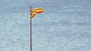 Katalonya bayrağı mavi denizin arka planında rüzgarda dalgalanıyor. Güneşli bir yaz gününde rüzgar. Sarı ve kırmızı çizgili bayrak. Su yüzeyinde hafif dalgalanmalar. Avrupa 'da turizm.