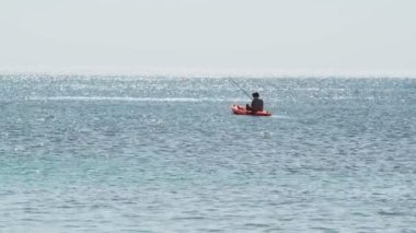 Kırmızı şişme bir teknede balıkçı açık denizde balık tutuyor. Işık dalgaları ve güneş mavi suda parlıyor. Sıcak, güneşli bir gün. Yaz soğuğu. Deniz kenarında tatiller. Deniz ürünleri. Rahatla ve sakinleş.