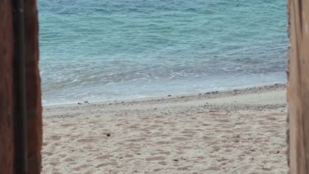 Piękny widok na plażę ze starego kamiennego pasa. Mała wioska nad morzem. Małe fale łagodnie wpadają na piaszczystą plażę. Czysta niebieska woda i miękki piasek. Letni słoneczny dzień. Lekka bryza. Lato chłodne — Wideo stockowe