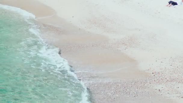 Piękne miękkie fale przebiegają przez skały i piasek. Przezroczysta niebieska woda z odblaskiem słońca. Letni słoneczny dzień. Wakacje nad morzem. Spokój i relaks. Wspaniały widok na morze. — Wideo stockowe