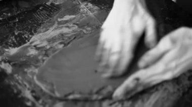 Çamurla çalışan kadın ellerinin yakın çekimi. Potter heykel yapma sürecinde. Kil ürünü şekillendirmek. Kara çamur. Siyah beyaz video. Çömlek atölyesi. Sanatçı koyu plastik bir kütleden heykel yapıyor..