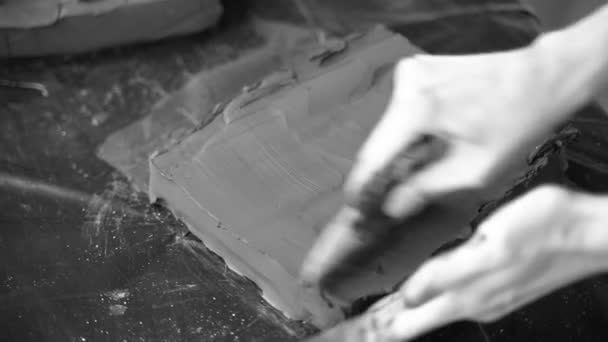 Närbild av kvinnliga händer som arbetar med lera. Potter på väg att skulptera. Forma en lerprodukt. Mörk lera. Svart och vit video. Krukverkstad. Konstnären skulpterar från en mörk plastmassa. — Stockvideo