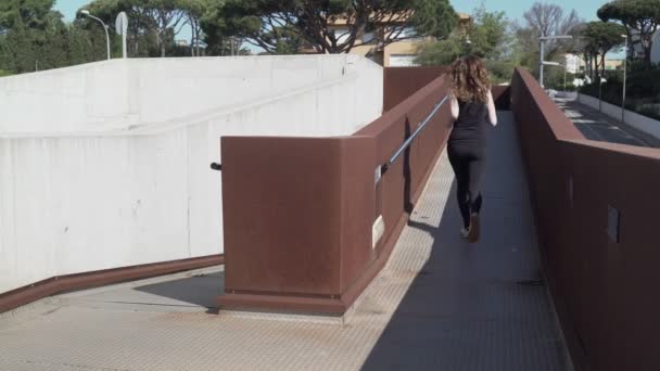 Femme aux cheveux longs en leggings noirs faisant du jogging dans un beau paysage urbain. Course matinale en ville. Sport et mode de vie sain. Athlète. Sport urbain. Exercice en plein air par une journée ensoleillée. — Video