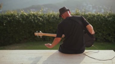 Siyah tişörtlü ve siyah şapkalı adam bas gitar çalıyor. Müzisyen ve gri Fransız bulldog 'u güzel manzaralı terasta. Bas gitarist köpeğiyle altın akşamın tadını çıkarıyor. Evcil hayvan 