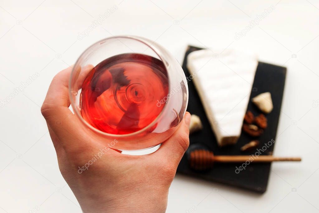 Glass with rose wine in a female hand. Someone drinks wine and eats French brie cheese.