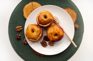 Beyaz bir tabakta fındık, kuru üzüm ve bal ile doldurulmuş fırında elma. Yeşil tabak tutacağı.