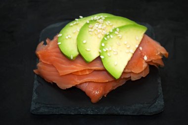 Taze somon, levhada avokado, siyah beton arka plan. Çiğ somon tartar..