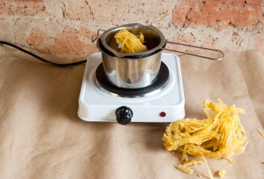 Büyük mumlar yapmak için ham balmumu. Ev yapımı mum. Eriyip sıvıya dönüşme sürecinde. Elektrikli ocağın üzerinde metal bir kasede. .