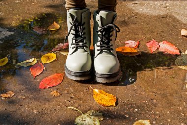 Sonbahar havası. Havalı sonbahar ayakkabıları giyen bir kız yağmurdan sonra su birikintisinde duruyor. Düşen sonbahar bir su birikintisine dökülüyor.. 