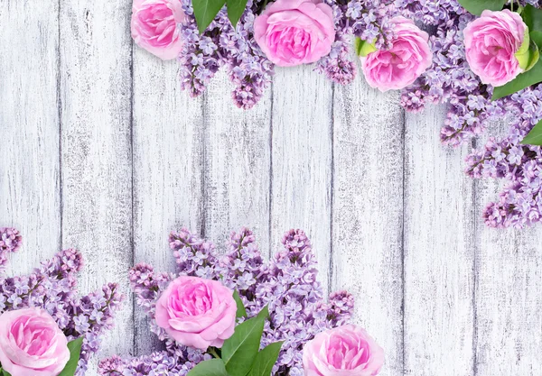 ぼろぼろの木板の背景にバラとライラックの花 — ストック写真