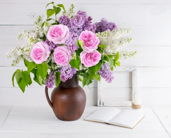 Lilac bouquet and roses in clay jug with open book and candle in — Stock Photo, Image