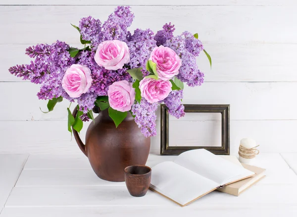 Buquê de lilás e rosas em jarro de barro com livro aberto e vela em — Fotografia de Stock