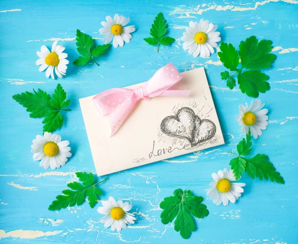 Daisies and postcard with painted hearts and bow — Stock Photo, Image