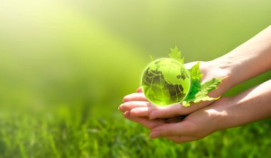Toprak kristal küre küresi ve akçaağaç yaprağı insan eliyle çimen arka planında. Çevreyi kurtarmak, temiz yeşil gezegeni kurtarmak, ekoloji kavramı. Dünya Günü için Kart.