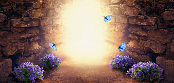 Photo background with magical trail leading through stone dungeon cave towards mystical glow, fantastic bluebells campanula flowers, flying blue butterflies. Fairytale tranquil fantasy scene, empty space.