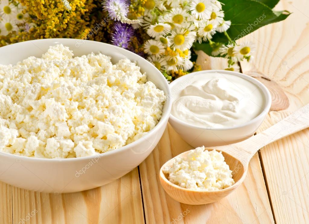 Cottage cheese in bowl with wooden spoon and sour cream