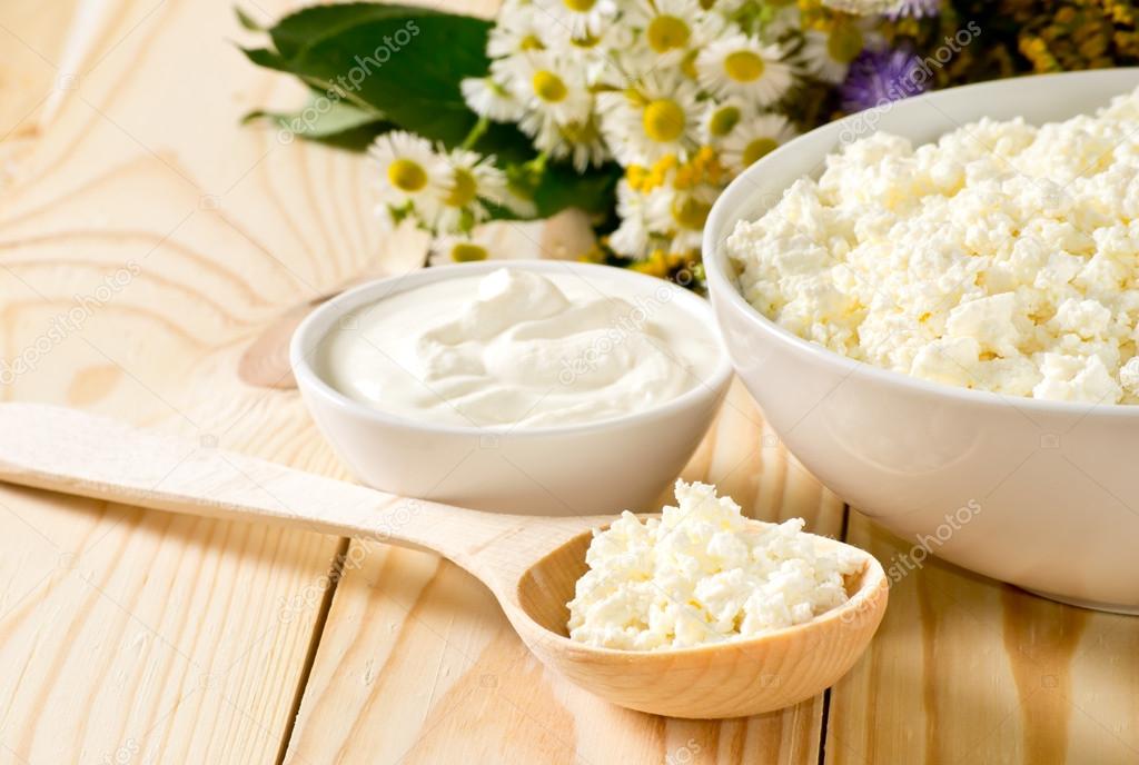 Cottage cheese in bowl with wooden spoon and sour cream