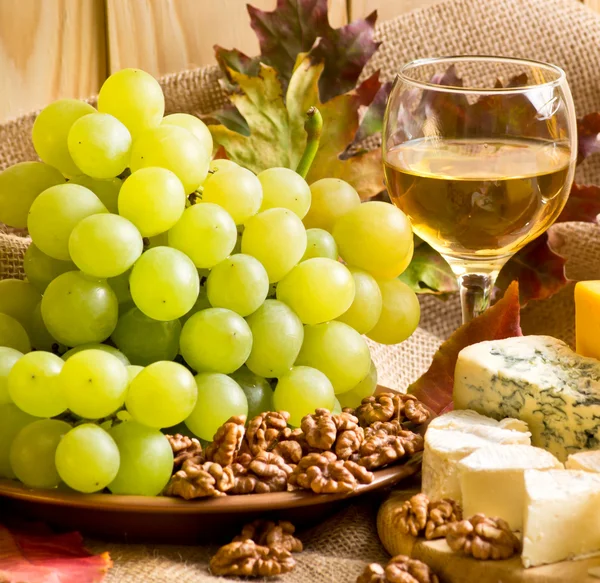 Vino blanco con queso, nueces y uvas sobre saco — Foto de Stock