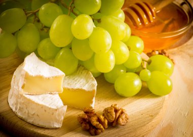 Still life of cheese, honey, walnuts and grapes clipart