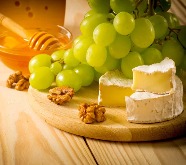 Still life of cheese, honey, walnuts and grapes — Stock Photo, Image