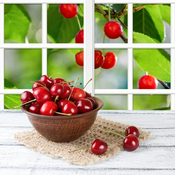 Sweet cherry on the wooden board and garden outside the window — Stock Photo, Image
