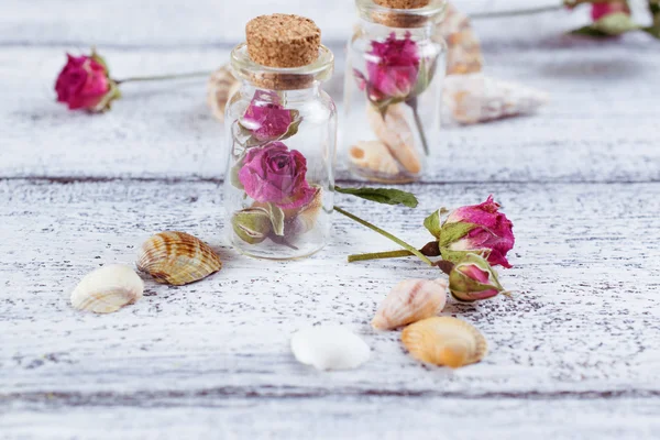 Kleine glazen fles gevuld droge rozen en schelpen — Stockfoto