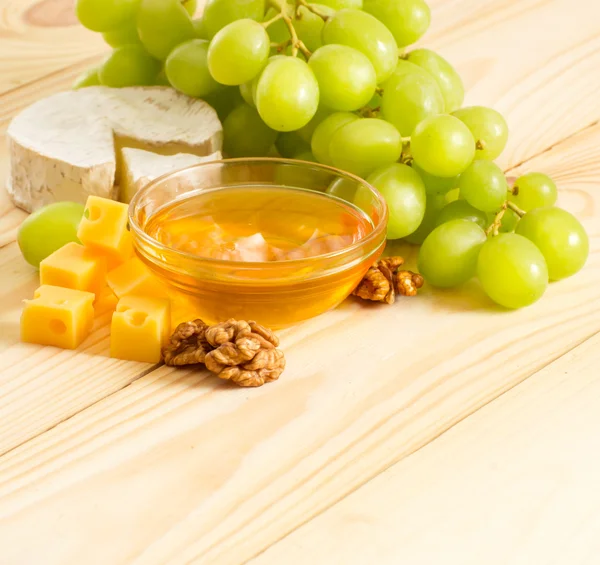 Still life of cheese, honey, walnuts and grapes — Stock Photo, Image