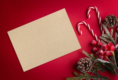 Noel kırmızı arka planı, boş kağıt, noktalı kalem, dekoratif köknar dalı, ağaç süslemesi için şeker kamışı ve koni. Dekorlu ve kopya alanı olan yeni yıl kış tatili kompozisyonu, üst görünüm.