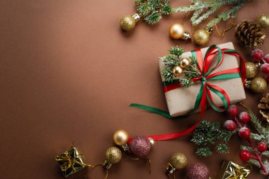 Noel arkaplanı, fiyonklu el yapımı hediye kutusu, ağaç süslemesi için dekoratif köknar dalı, top ve koni. Yeni yıl bayramı süsleri, hediyeler, dekorasyon ve metin için kopya alanı, üst görünüm.