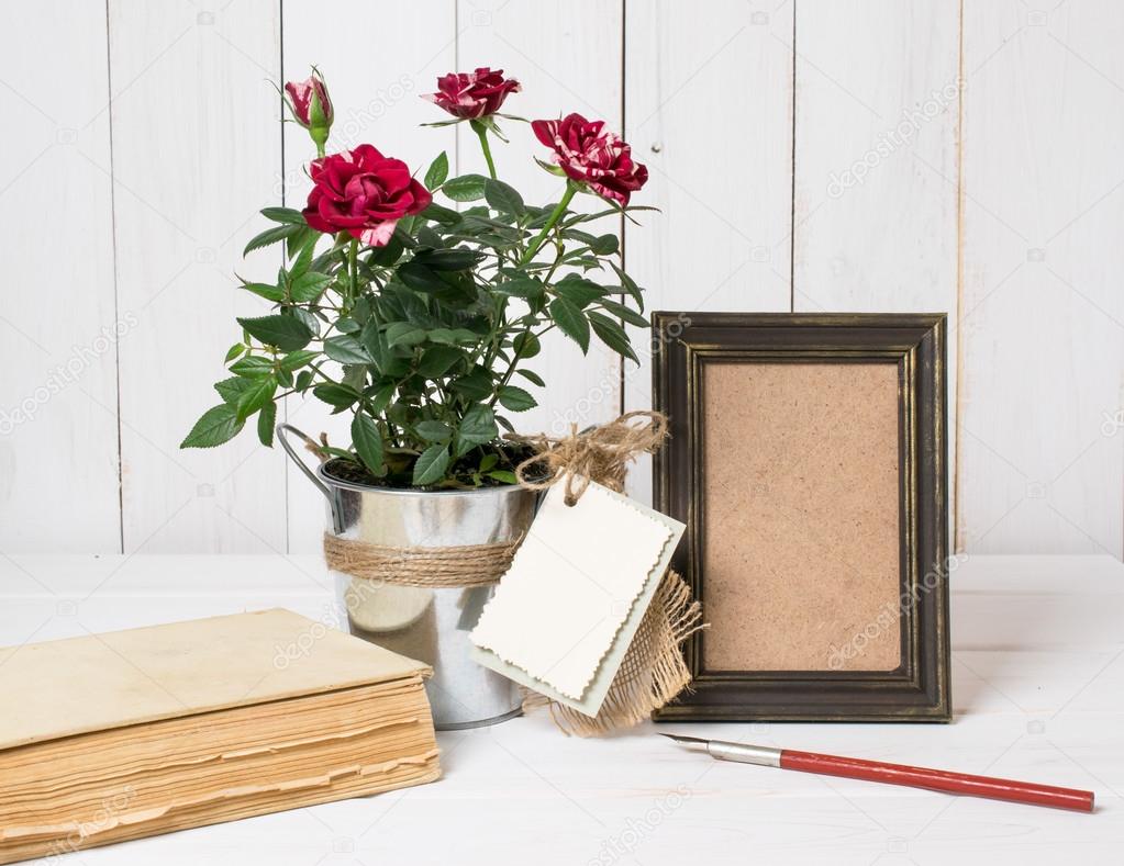 Retro photo frame and old pen with roses bouquet on wooden board