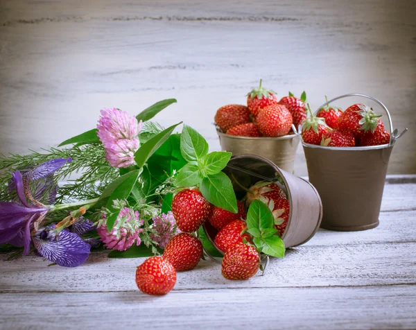 Strawberry in a bucket and flowers — Stock Photo, Image