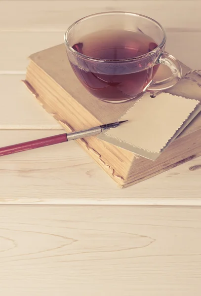 Стара книга з декоративною вітальною листівкою, ручкою і чашкою чаю — стокове фото