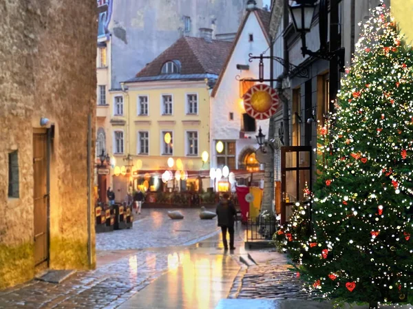 雨の通りのクリスマスツリー照明人々はエストニアの中世タリン旧市街の休日の舗装上のぼやけた夜の光の反射を歩く — ストック写真
