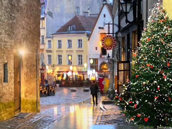 ヨーロッパのクリスマス休暇雨の通りのクリスマスツリー照明人々はエストニアの中世タリン旧市街の休日の舗装上のぼやけた夜の光の反射を歩く — ストック写真