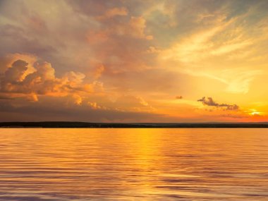  Altın tropikal gün batımı deniz yansıması su dalgası, akşam gökyüzünde dramatik kabarık bulutlar ve arazi doğasında yeşil çimenler. 