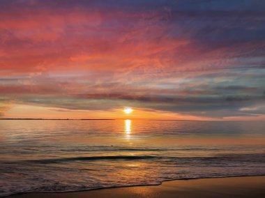   Deniz batımında güzel bir gün batımı pembe altın sarısı bulutlar üzerinde mavi mavi gökyüzü yarı akşam, su dalgası doğa manzarası yansıması