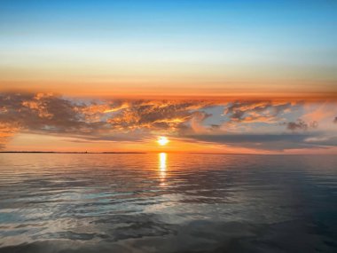   Deniz batımında güzel bir gün batımı pembe altın sarısı bulutlar üzerinde mavi mavi gökyüzü yarı akşam, su dalgası doğa manzarası yansıması